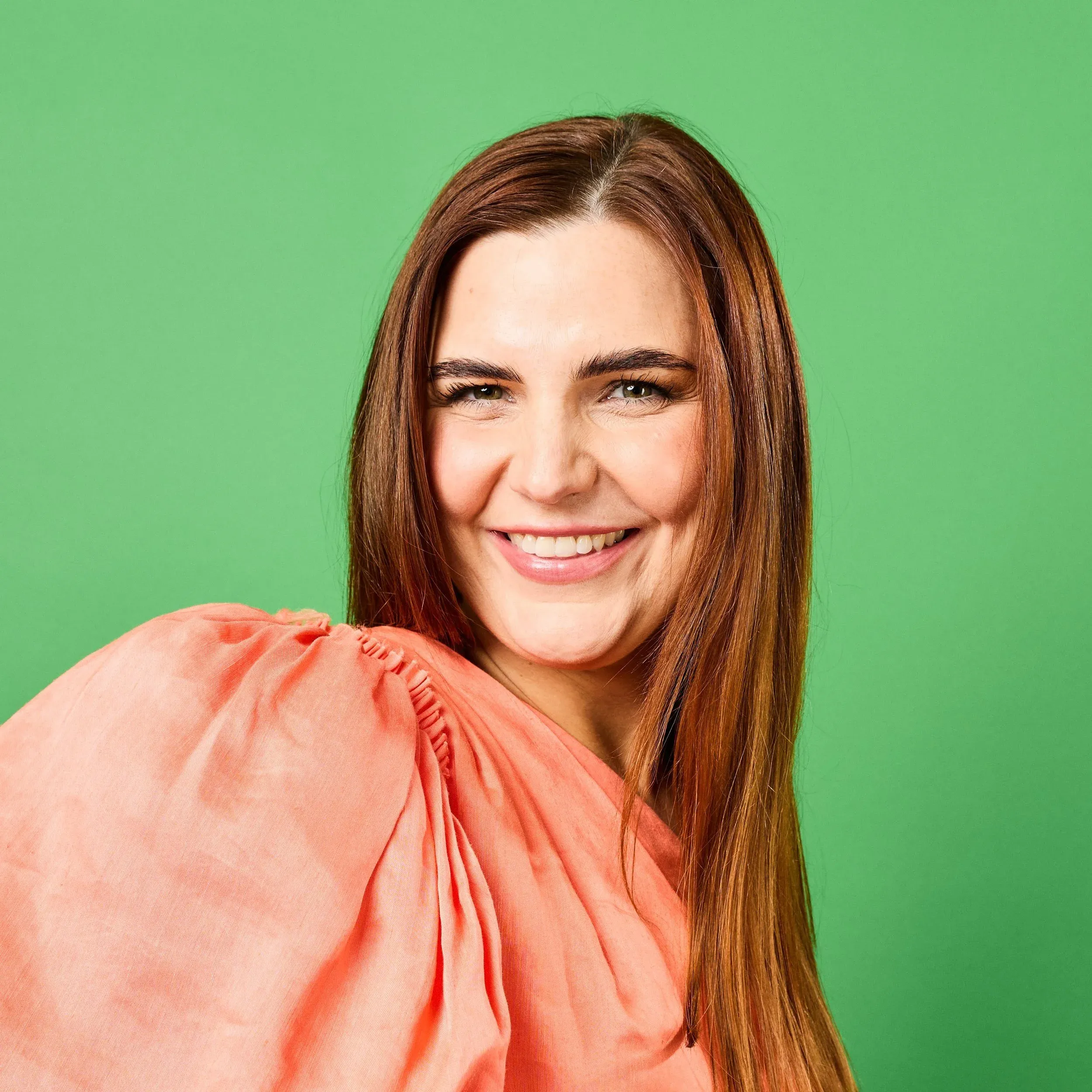 Dr Sylvia Ross smiling in an orange blouse against a green background