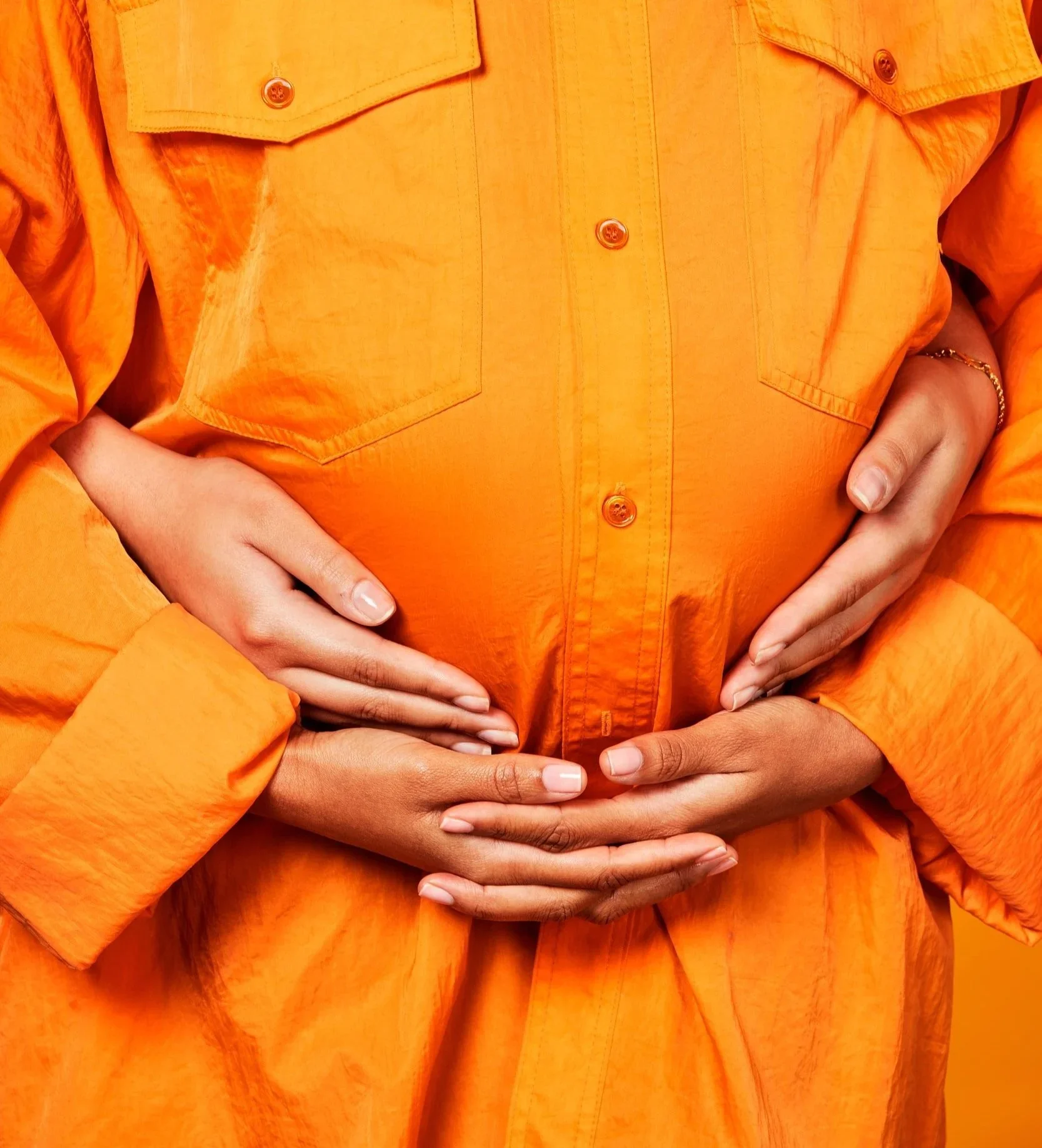 Two pairs of hands cradling a pregnant belly in an orange utility shirt