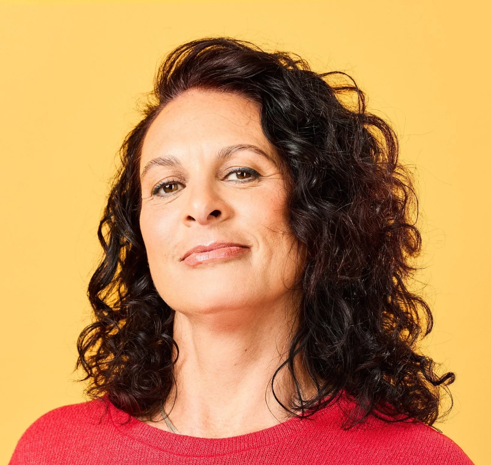 Dr Michal Amir with dark curly hair and a red top against a yellow backdrop