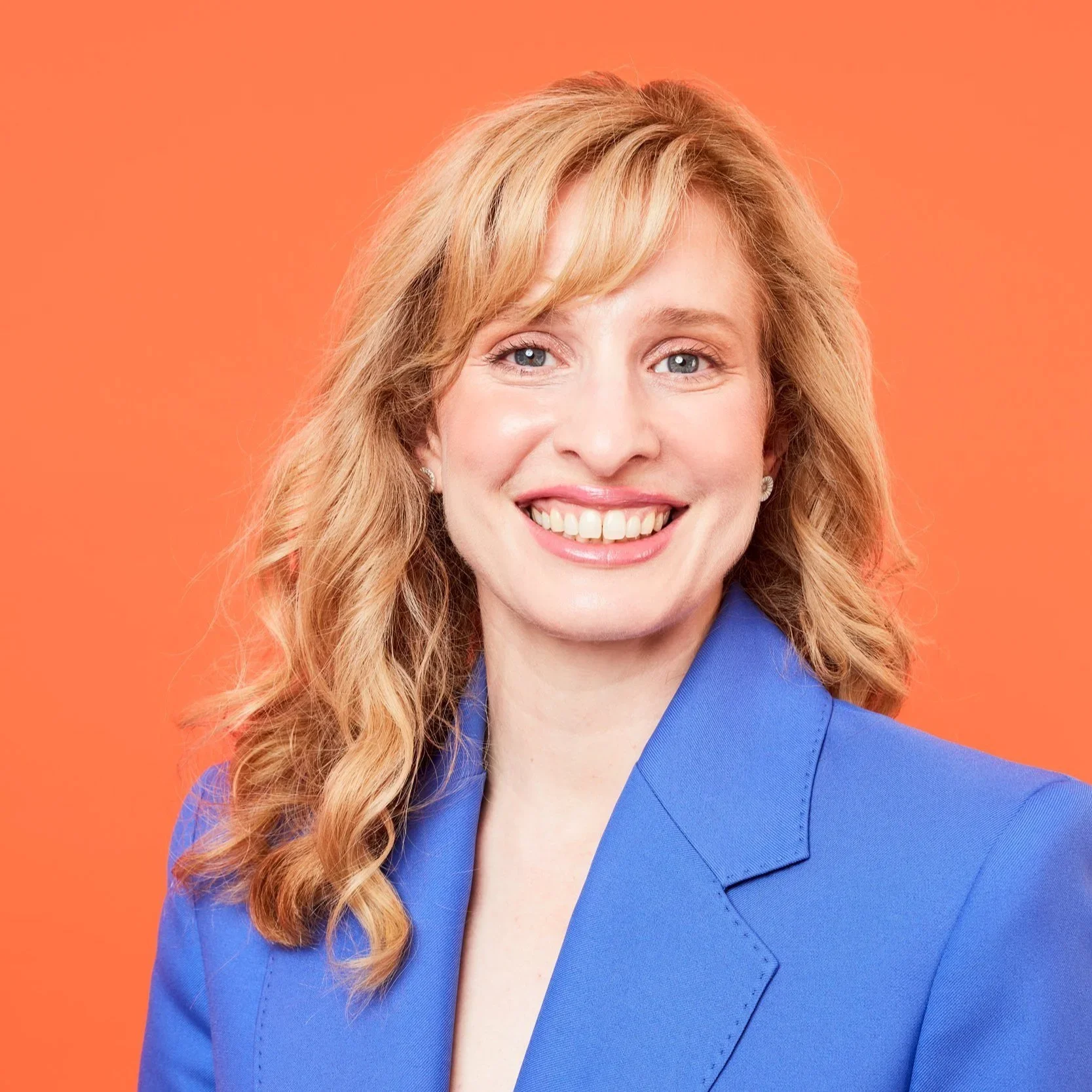 Dr Raelia Lew smiling in a royal blue blazer against an orange backdrop