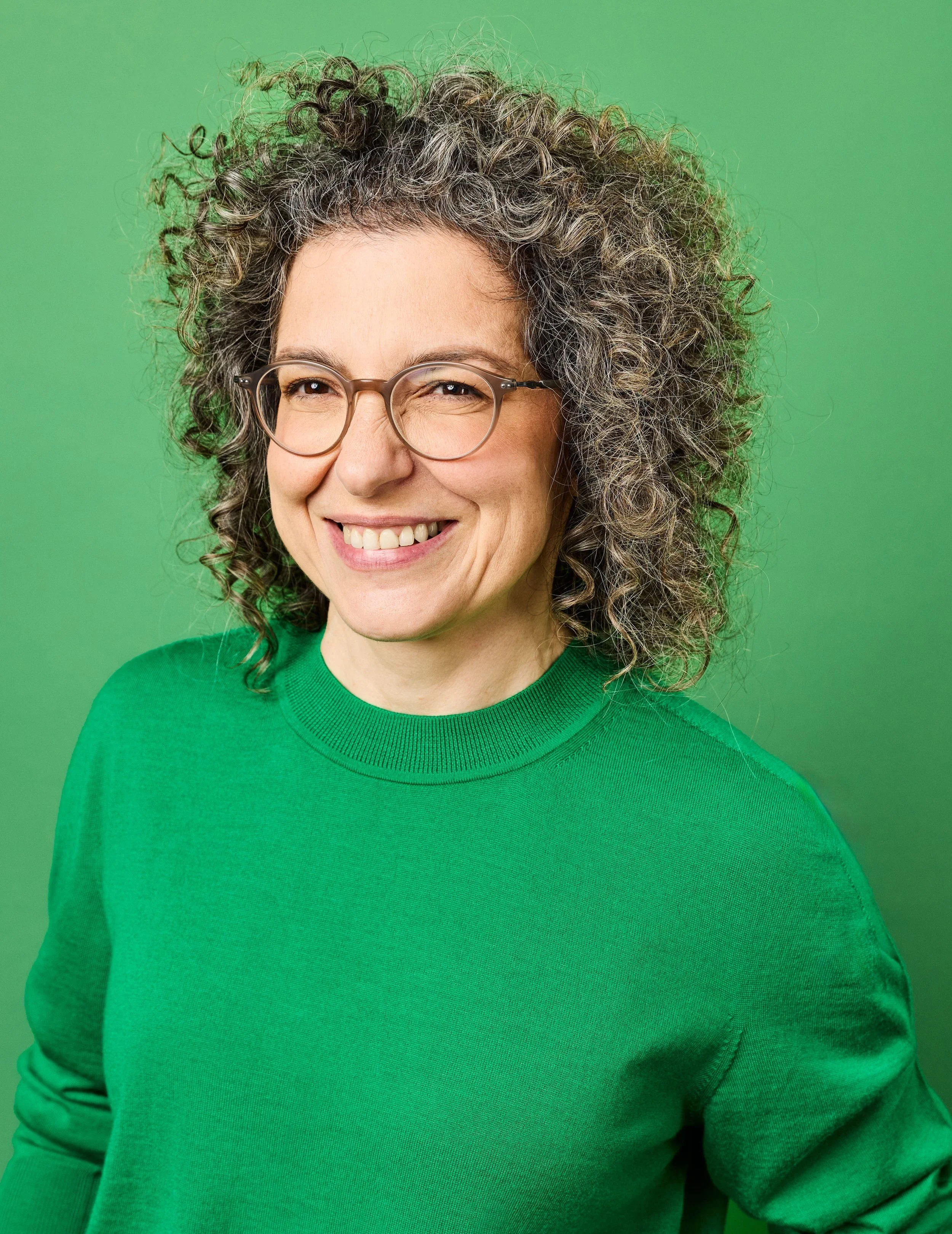 Dr Tzippora Ben-Harim smiling in round glasses and a green jumper