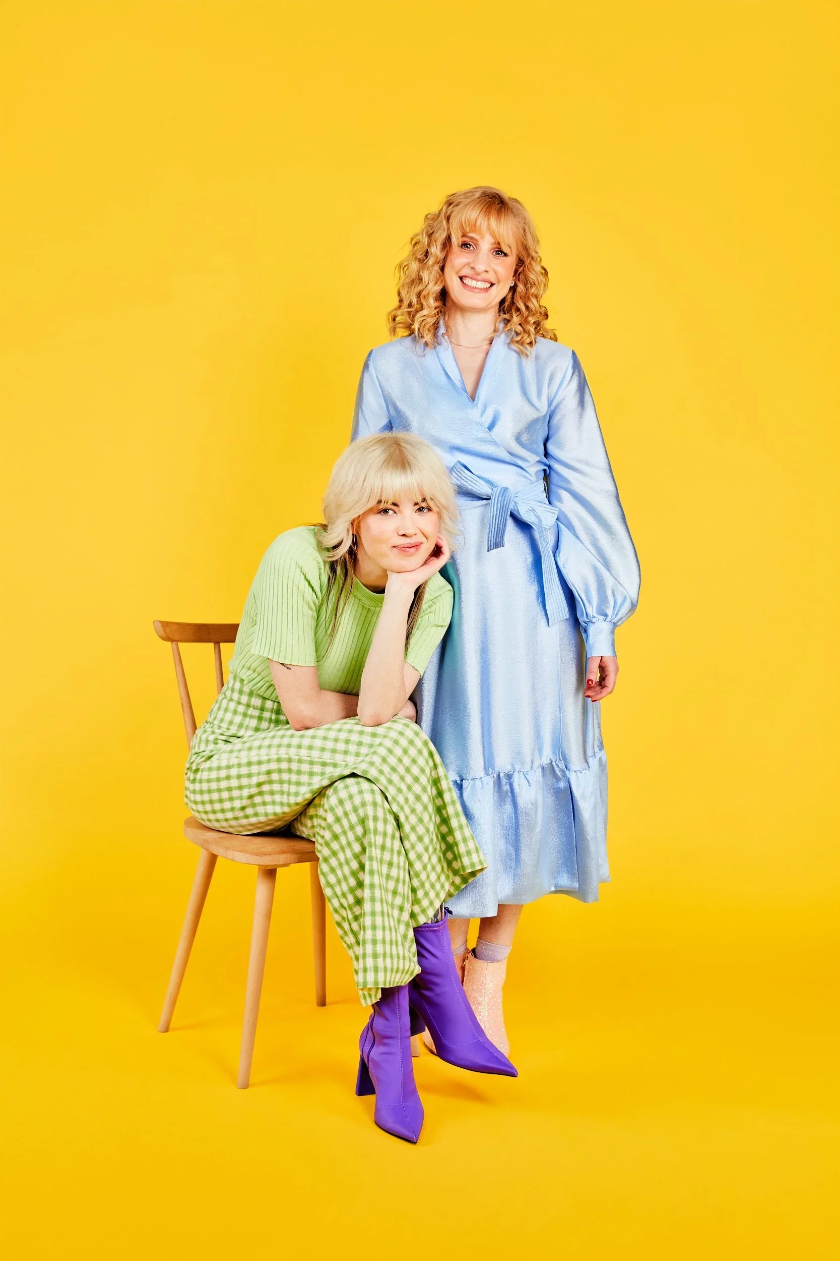 Dr Raelia Lew in a pale blue wrap dress standing behind a seated woman in a green gingham outfit